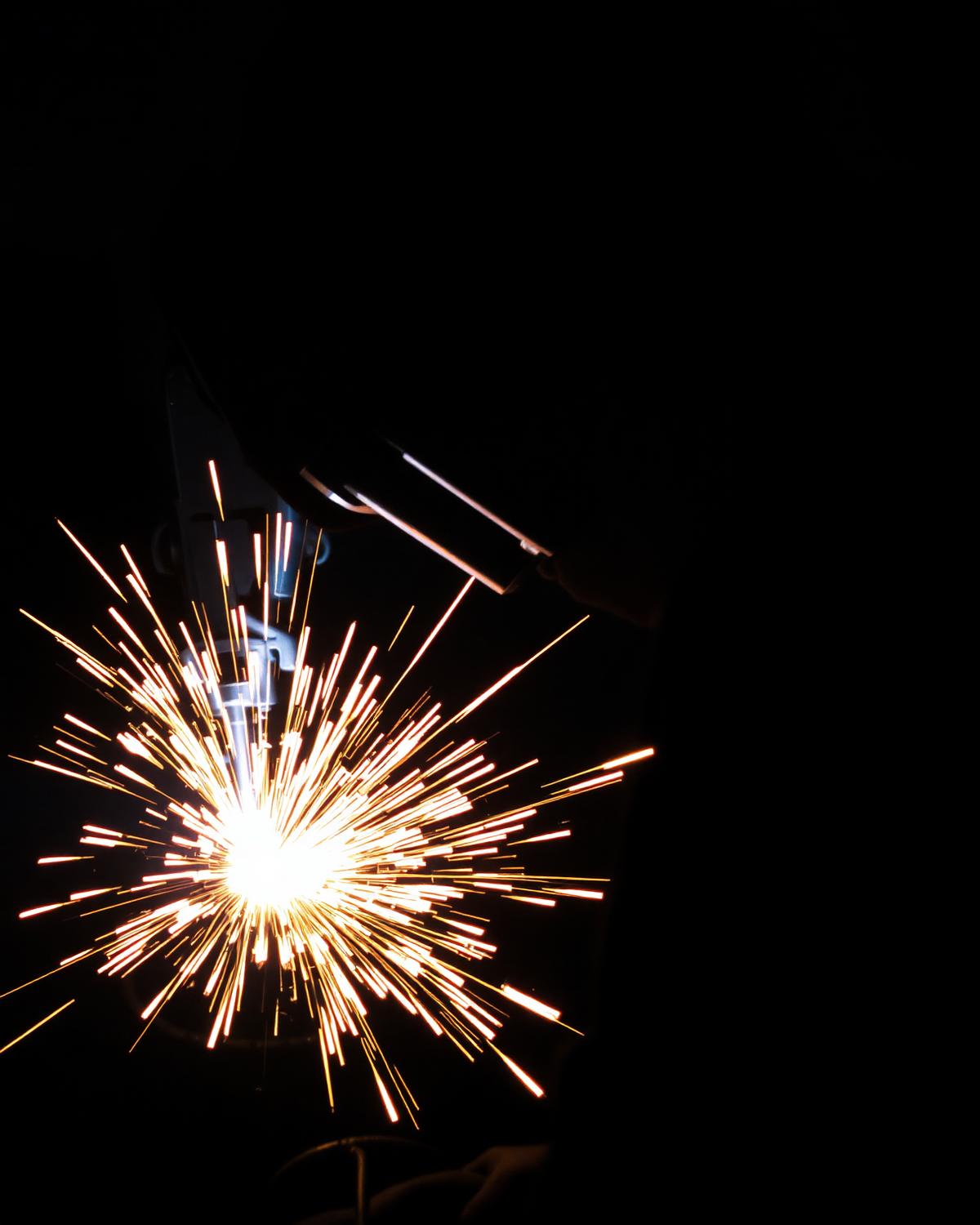 Steel fabrication welding sparks illuminating a dark workshop